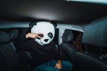 Uomo indossando panda maschera testa seduto sul sedile posteriore della macchina e mostrando gesto di pace . — Foto stock