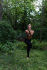 Vista frontal de chica en forma realizando yoga asana sobre césped entre bosques - foto de stock