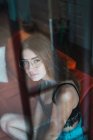 Brünettes Mädchen mit Brille posiert hinter Glas und schaut in die Kamera — Stockfoto