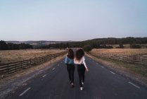 Вид сзади на девушек, идущих по сельской дороге — стоковое фото
