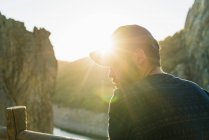Retrato de homem vestindo boné olhando sobre o ombro no terraço rochoso iluminado pelo sol — Fotografia de Stock