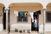 Goree, Senegal- 6 dicembre 2017: Uomo africano in porta di casa povera con biancheria appesa alla luce del sole . — Foto stock