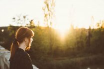 Вид збоку дівчина-імбир позує на сільському мосту на сонячному світлі — стокове фото