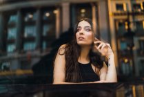 View through window to brunette girl posing at cafe table and looking away — Stock Photo