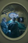 Vue à travers le verre dans la porte du personnel médical travaillant avec le patient dans la salle d'opération — Photo de stock