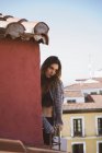 Ritratto di ragazza bruna in alto e cardigan in posa sul balcone sopra i tetti della città — Foto stock