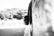 Goree, senegal- 6. Dezember 2017: Seitenansicht eines fröhlichen afrikanischen Jungen, der an der Wand hängt und in die Kamera blickt — Stockfoto