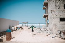 Back view of man walking on sandy construction site with grungy exterior on background of ocean. — Stock Photo