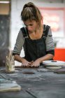 Portrait of female potter forming clay stick on wooden table at workshop — Stock Photo