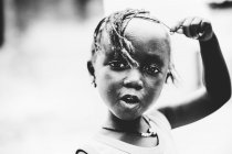 Goree, Senegal- Dezembro 6, 2017: Retrato de menina africana bonito brincando com o cabelo e olhando para a câmera . — Fotografia de Stock