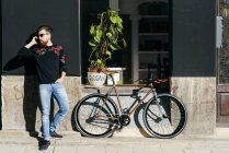 Uomo di tendenza in piedi in bicicletta e parlando su smartphone — Foto stock