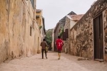 Goree, Senegal- 6 de dezembro de 2017: Vista traseira de dois meninos africanos andando ao longo da rua na pequena cidade africana . — Fotografia de Stock