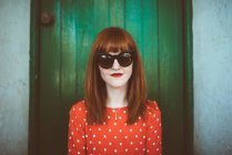 Portrait of redhead woman in red clothing and sunglasses posing over green wooden wall — Stock Photo