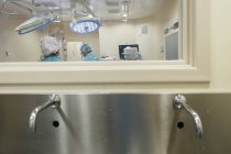 Girato attraverso vetro di operatori medici in sala operatoria procedura di conduzione . — Foto stock