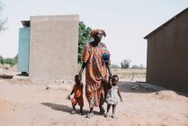 Goree, Senegal- 6 dicembre 2017: Donna africana che si tiene per mano dei bambini mentre cammina sulla sabbia della strada in campagna povera . — Foto stock