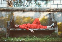 Вид збоку молода руда пристрасна жінка в червоному лежить на гранжевій кам'яній лавці — стокове фото