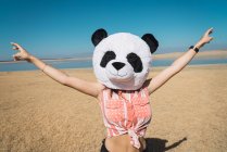 Woman with panda toy head posing on desert lake shore with outstretched hands — Stock Photo