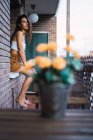 Side view of brunette model sitting on windowsill at balcony and looking at camera — Stock Photo