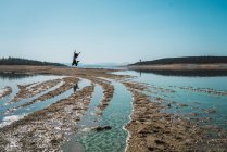 Далекий взгляд на женщину, прыгающую через грязную местность с озерной водой — стоковое фото