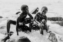 Goree, senegal- 6. Dezember 2017: lachende schwarze Jungen sitzen auf Felsen im plätschernden Wasser des Ozeans im Sonnenlicht. — Stockfoto