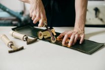 Crop shot of workman using tools and gold material while imprinting on leather. — Stock Photo