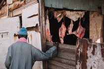 Visão traseira do homem em pé na entrada do estábulo com carne pendurada — Fotografia de Stock