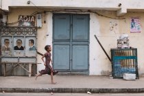 Goree, Senegal- 6 de dezembro de 2017: Vista lateral da menina africana correndo ao longo da rua da pequena cidade africana . — Fotografia de Stock