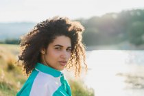 Curly woman posing on nature in sunlight and looking at camera — Stock Photo