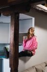 Vista lateral da menina em suor rosa posando em casa com café — Fotografia de Stock