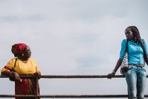 Goree, Senegal- Dezembro 6, 2017: Mulher africana em roupas tradicionais olhando para a jovem mulher em roupas modernas e de pé perto da cerca . — Fotografia de Stock