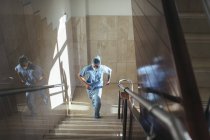 Vista de ángulo bajo del hombre en uniforme corriendo escaleras arriba en el hospital - foto de stock