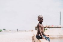 Goree, Senegal- 6 dicembre 2017: Piccolo ragazzo senza maglietta seduto a guardare la macchina fotografica . — Foto stock