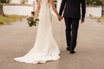 Coltiva sposa e sposo tenendosi per mano e camminando per strada — Foto stock