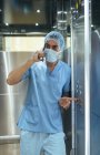Homme en uniforme de médecin debout dans l'ascenseur de l'hôpital et parlant sur smartphone
. — Photo de stock