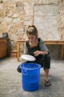 Front view of female potter squatting over bucket and moistening plate — Stock Photo