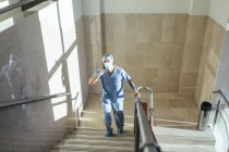 Homem de uniforme médico falando ao telefone e subindo escadas no hospital — Fotografia de Stock