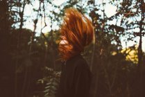 Vue latérale de la rousse femme agitant les cheveux sur fond de nature — Photo de stock