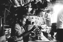 Goree, senegal- 6. Dezember 2017: Seitenansicht eines Mannes, der mit einer alten Nähmaschine am Tisch in der Werkstatt sitzt und . — Stockfoto
