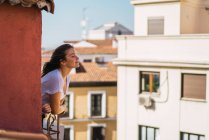 Вид сбоку девушки-брюнетки, наклоняющейся с балкона и наслаждающейся новым днем — стоковое фото