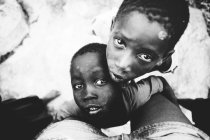 Goree, Senegal- 6 de diciembre de 2017: Retrato de bajo ángulo de niños abrazando rodillas de fotógrafo y mirando a la cámara . - foto de stock