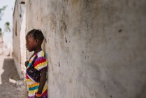 Йофф, Сенегал - 6 декабря 2017 года: Вид сбоку на девушку в ярком платье, стоящую возле бетонной стены в солнечный день . — стоковое фото