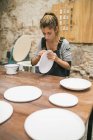Концентрований гончар сидить за столом і формує тарілки з білої глини . — стокове фото