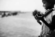 Goree, Senegal- Dezembro 6, 2017: Vista lateral da menina de pé com ouriços do mar na costa . — Fotografia de Stock