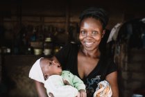 Goree, Senegal- 6 de diciembre de 2017: Retrato de una mujer africana sosteniendo al bebé y sonriendo felizmente a la cámara . - foto de stock