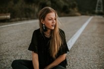 Stilvolle junge Frau sitzt am Straßenrand — Stockfoto