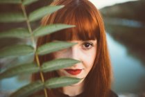 Portrait redhead woman covering eye with green leaves — Stock Photo