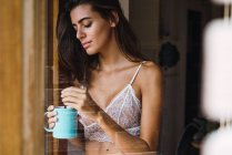 Bruna ragazza in reggiseno appoggiato sulla finestra e bere caffè — Foto stock