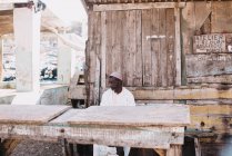 Goree, Senegal- 6 dicembre 2017: uomo africano seduto vicino a una bancarella di legno in strada nel quartiere povero della città . — Foto stock