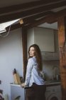 Sensual menina morena em roupas casuais inclinando-se no balcão da cozinha e olhando sobre o ombro na câmera — Fotografia de Stock