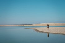 Silhouette of woman walking on shore of turquoise lake — Stock Photo